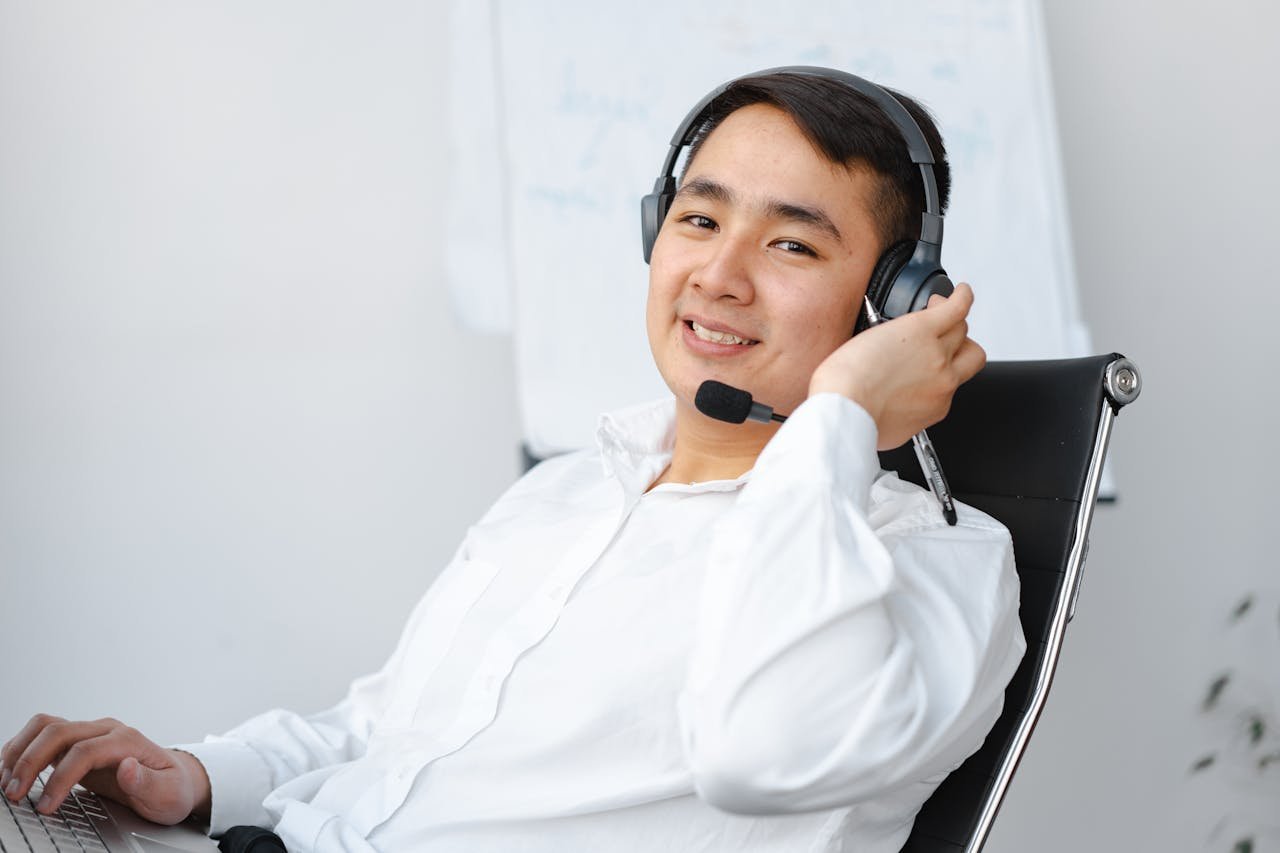 Asian call center agent sitting at desk with headset, smiling.